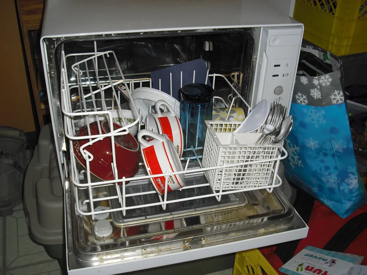 Small dishwasher standing open with plates in the racks and a cutlery basket