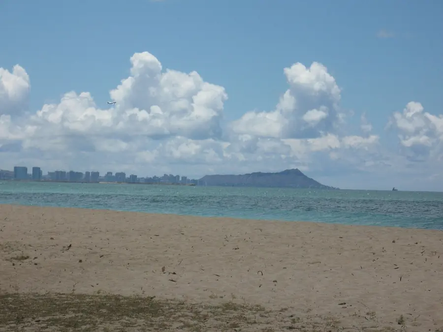 Sandy shoreline at Ewa Beach looking east toward Diamond Head, with trade-wind clouds overhead