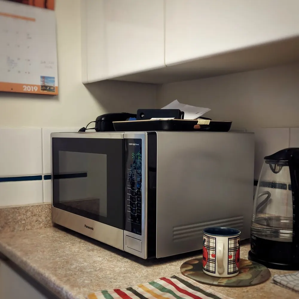 Stainless microwave on a counter next to a kettle and a mug