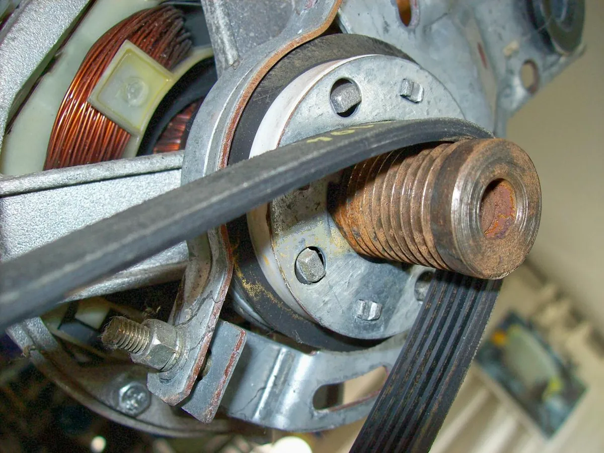 Close view of a motor pulley driving a ribbed belt inside an appliance