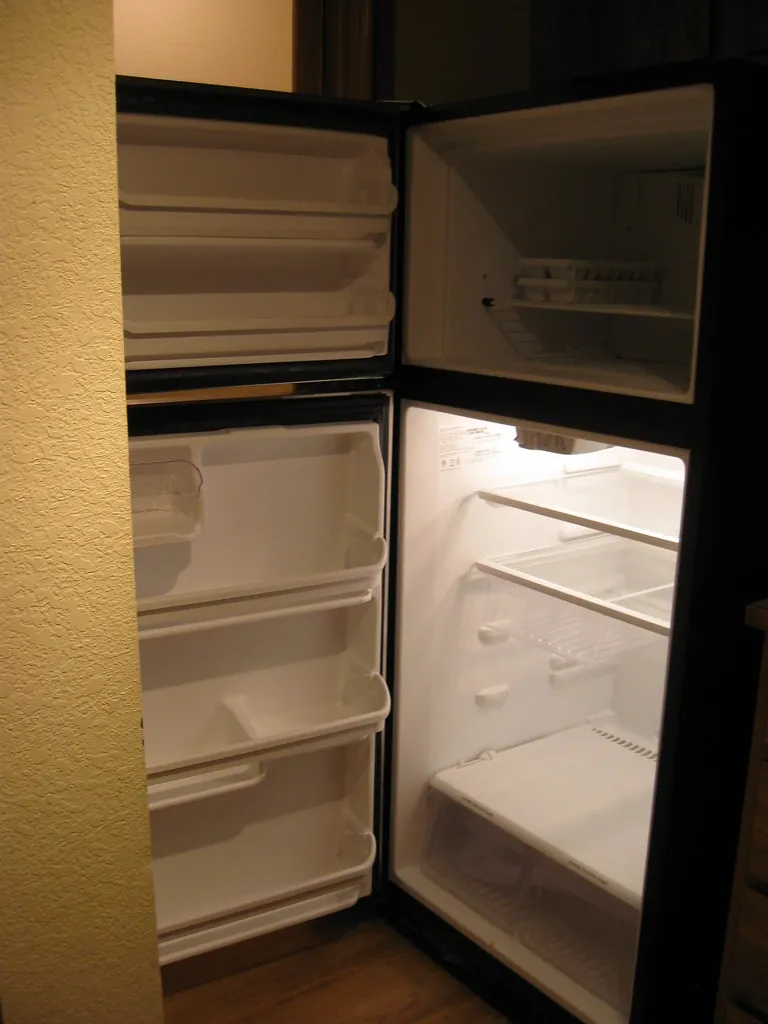 Refrigerator standing open with bare glass shelves, crisper drawers and door bins