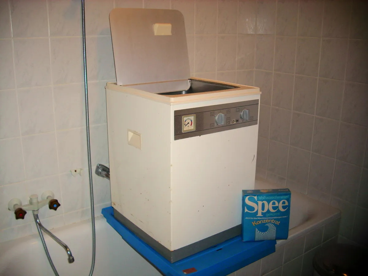 Small top-load washing machine with its lid open in a tiled laundry room